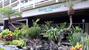A hotel named 'Island Colony' with a sign above the entrance, a small waterfall feature, and various tropical plants in the foreground. - High-Floor Waikiki Apt w/ Views & Pool (Honolulu)