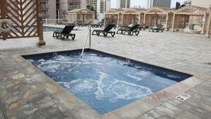 A hot tub area with lounge chairs, a pool, and a stone-tiled floor. - High-Floor Waikiki Apt w/ Views & Pool (Honolulu)