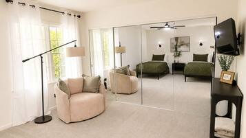 A bedroom with a bed, a chair, a desk, a mirror, and a TV.