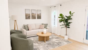 A living room with a sofa, two armchairs, a coffee table, a floor lamp, a large plant, and three framed pictures on the wall.