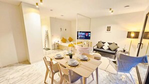 A modern living room with a sofa, a television, and a dining area with a table set for four. - Cosy Terrace Studio close to city center (Luxembourg City)