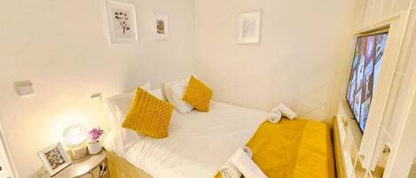 Una habitación de hotel ordenada con una cama, una mesita de noche con lámpara y un televisor instalado en la pared.