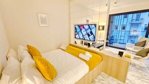 A hotel room with a bed, a TV, a desk, and a view of the city. - Cosy Terrace Studio close to city center (Luxembourg City)
