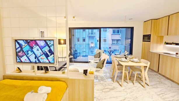 A modern hotel room with a bed, a TV, a dining area, and a balcony with a city view. - Cosy Terrace Studio close to city center (Luxembourg City)