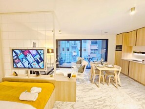 Een moderne hotelkamer met een bed, een televisie, een zithoek en een balkon met uitzicht over de stad.