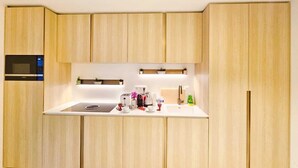 A modern kitchen with wooden cabinets, a built-in microwave, a white countertop, and a small shelf with plants. - Cosy Terrace Studio close to city center (Luxembourg City)