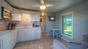 A modern kitchen with white cabinets, a tiled backsplash, and a built-in microwave. - 2 Cozy Cottages Fire Pit, Private Yards, Walkable Location in Spanish Village (Port Aransas)