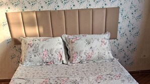 A neatly made bed with a floral bedspread, two pillows, and a folded towel on a green blanket. - A house to enjoy and take advantage of beaches, waterfalls, and many adventures in Ilhabela. (Ilhabela)