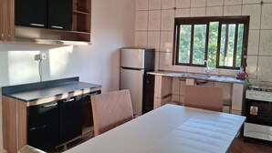 A compact kitchen with a dining table, a refrigerator, a stove, and a window with a view of greenery. - A house to enjoy and take advantage of beaches, waterfalls, and many adventures in Ilhabela. (Ilhabela)