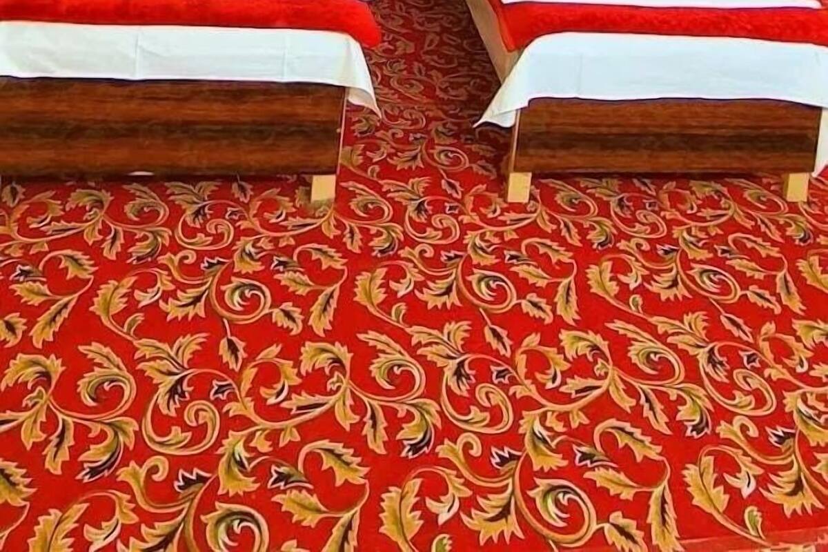 A hotel room with two beds, a red patterned carpet, and a large decorative wall hanging.