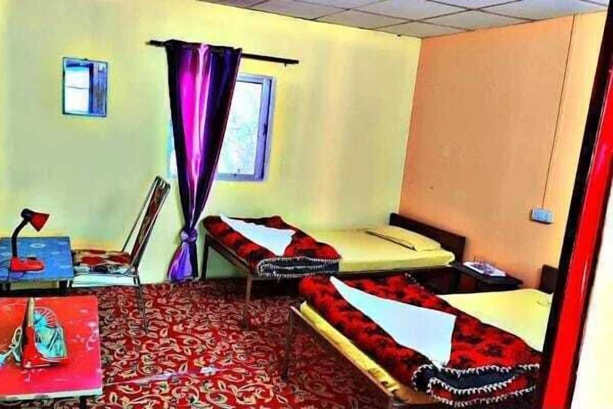 A room with two beds, a small table, a chair, and a window with curtains.