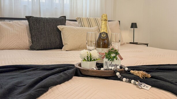A bed with a champagne bottle, glasses, a welcome mat, and a tray with flowers and a tag. - Modern Luxury Studio • Kitchen, Wi-Fi & Private Parking (Pembroke Pines)