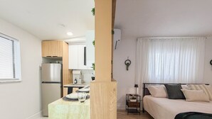 A compact living space with a kitchenette, a bed with multiple pillows, and a small bedside table. - Modern Luxury Studio • Kitchen, Wi-Fi & Private Parking (Pembroke Pines)