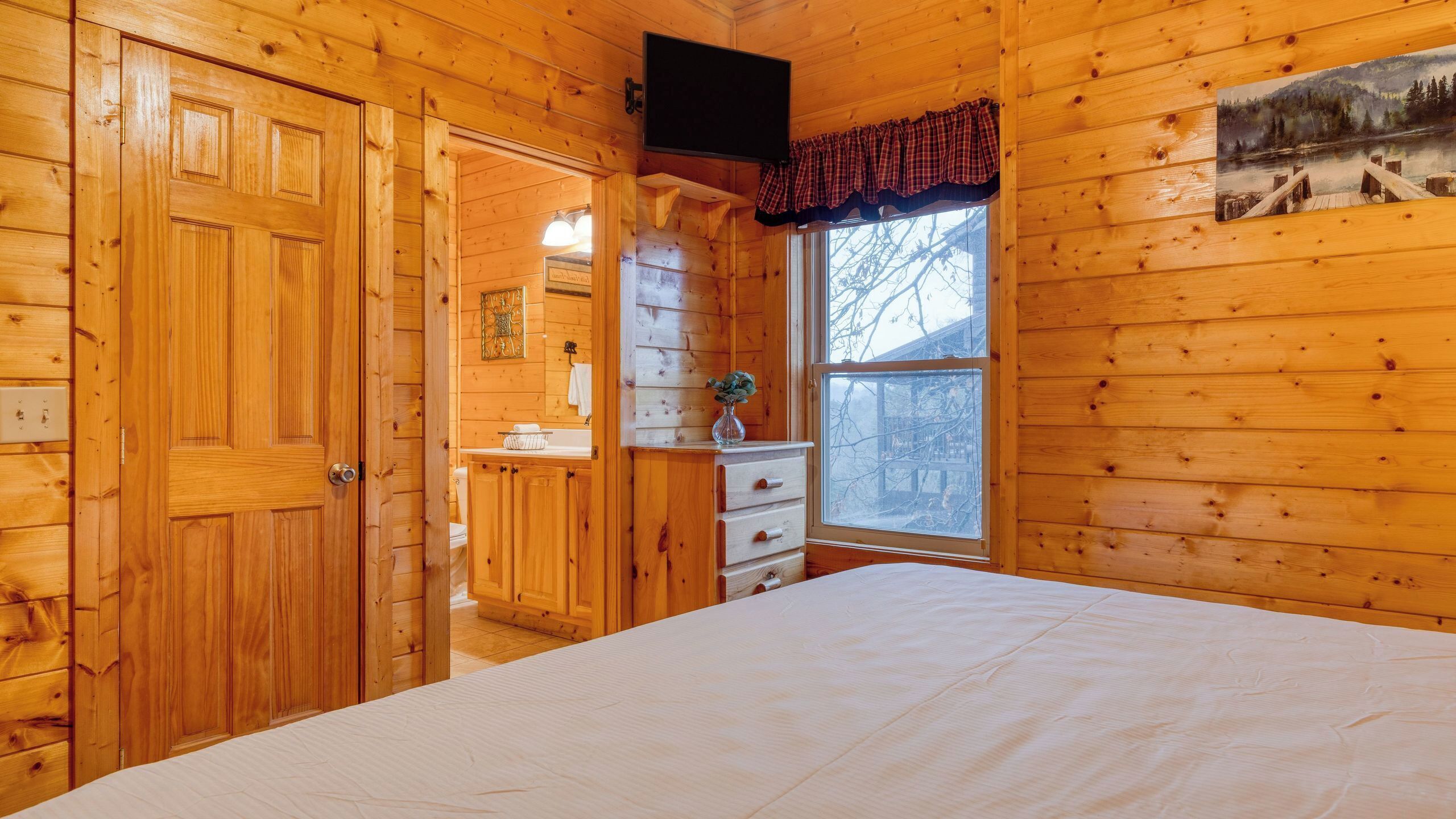 Interior de uma cabana de madeira com uma cama, cômoda e janela com vista.