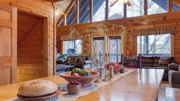 L’intérieur d’un chalet rustique, avec une table à manger en bois, un canapé et une grande fenêtre.