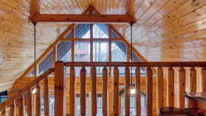 Un intérieur en bois avec un plafond en pente, un balcon doté de balustrades et une vue sur une maison à l’extérieur.
