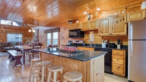 L’intérieur de la cabane est doté de murs en bois, d’une cuisine équipée d’appareils modernes, d’un coin repas avec une table et des tabourets en bois, et d’une grande fenêtre.
