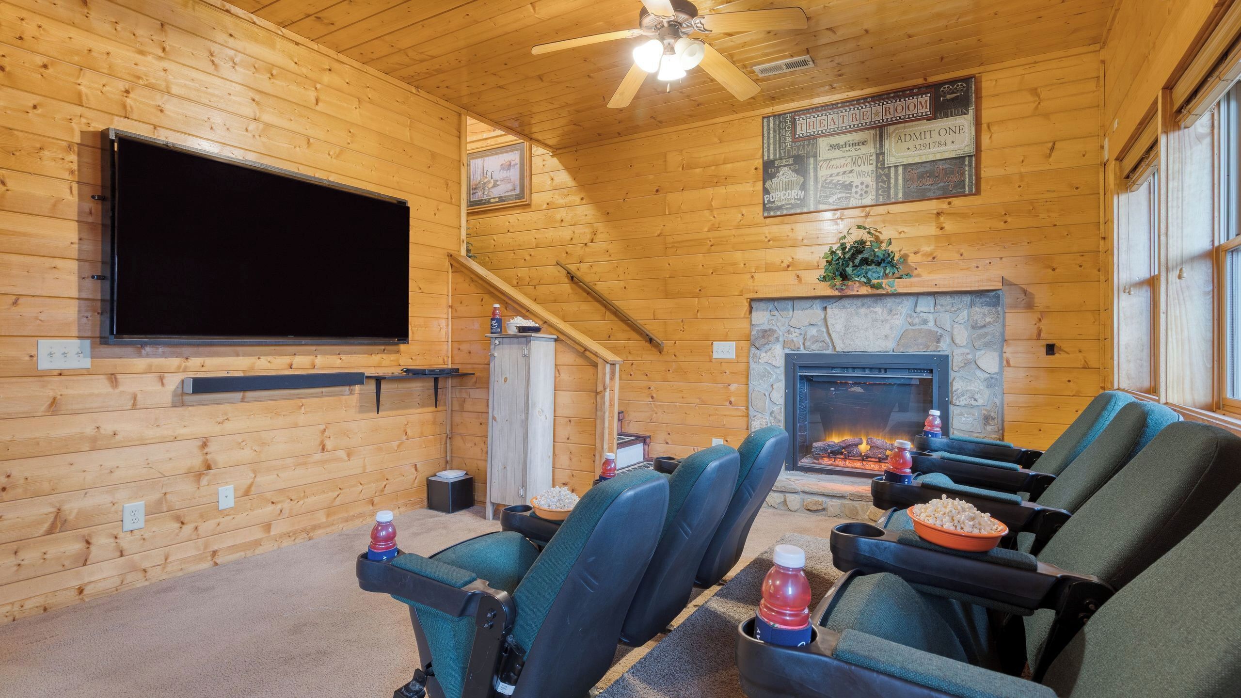 A cozy theater room with wooden walls, a fireplace, a flat-screen TV, and comfortable seating.