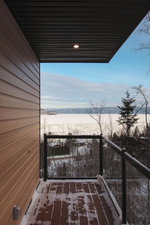 A wooden exterior wall, a metal railing, and a view of a snowy landscape with trees and mountains in the distance.