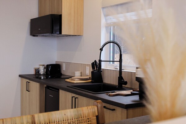 A modern kitchen with wooden cabinets, a black countertop, a sink, and a window with a view. - Refuge du Fjord (Saguenay)