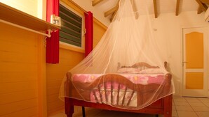 Un letto in legno con zanzariera, una tenda rossa e una finestra con persiane.