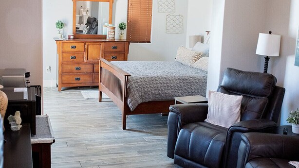 Een slaapkamer met een bed, een dressoir, een bureau, een leren fauteuil en een plafondventilator.