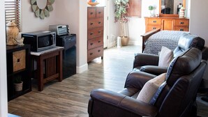 Een woonkamer met een leren bank, een houten salontafel, een plafondventilator, en een keuken met inbouwapparatuur en een houten kast.