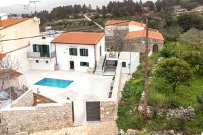 Un bâtiment blanc doté d’une piscine, de murs en pierre et d’un toit recouvert de tuiles rouges.