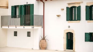 A white building with green shutters, a small balcony, and a tiled roof. - Traditional Anna's Stone House with Private Pool (Margarites)