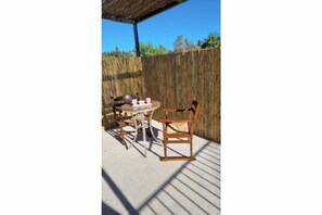 Une terrasse extérieure avec une table et deux chaises, une clôture en bois en arrière-plan et un ciel bleu dégagé.