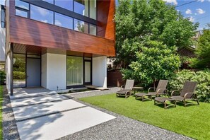 Ein modernes Haus mit überdachter Veranda, Sitzgelegenheiten im Freien und einem gepflegten Rasen.