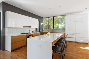 A modern kitchen with white cabinets, a wooden island, and a large window providing natural light. - Axiom Haus (Atlanta)