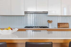 Une cuisine moderne avec des armoires blanches, une hotte de cuisinière en acier inoxydable et un plan de travail blanc.
