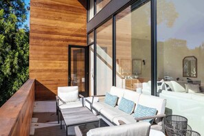 Un espace extérieur moderne, aménagé avec une terrasse en bois, des canapés blancs et des coussins à motifs.