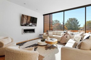 Ein modernes Wohnzimmer mit großem Fenster, Flachbildfernseher, einer Sofagarnitur und einem Couchtisch.