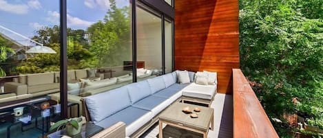 A modern outdoor seating area with a glass enclosure, wooden deck, and lush greenery.