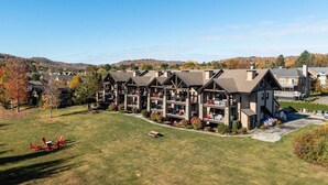 A multi-story hotel with a central courtyard, outdoor seating, and a view of the surrounding landscape. - Prestige Ski in Ski out Sommet Saint-Sauveur 3BR (Saint-Sauveur)