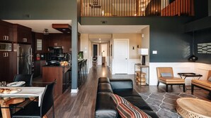 A modern kitchen with dark wood cabinets and stainless steel appliances, a dining area with a table set for two, and a cozy seating area with a sofa and chairs. - Prestige Ski in Ski out Sommet Saint-Sauveur 3BR (Saint-Sauveur)