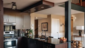 A modern kitchen with stainless steel appliances, a central island, and a wooden accent wall. - Prestige Ski in Ski out Sommet Saint-Sauveur 3BR (Saint-Sauveur)