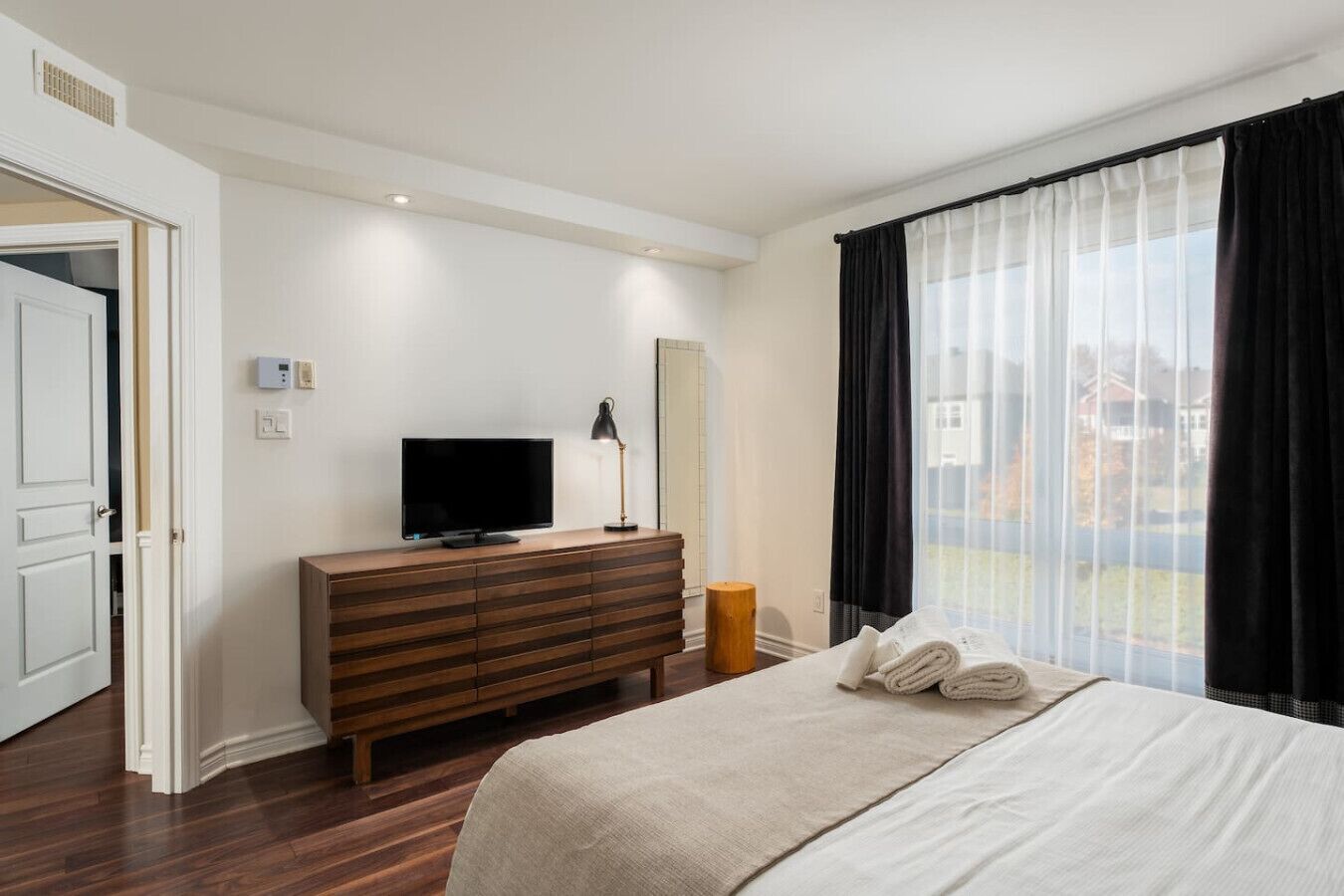Une chambre d’hôtel avec un lit, un téléviseur posé sur une commode en bois, une fenêtre avec des rideaux et une vue sur l’extérieur.
