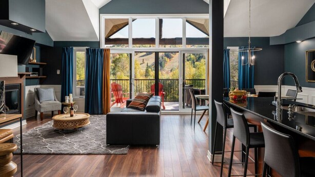 A modern interior with a large sliding glass door leading to a balcony, a kitchen area, and a seating area with a sofa and chairs. - Prestige Ski in Ski out Sommet Saint-Sauveur 3BR (Saint-Sauveur)