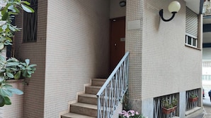 A building with a brick exterior, a staircase with a metal railing, and potted plants on the ground level. - Short Rent Milan Porta Romana  (Milan)