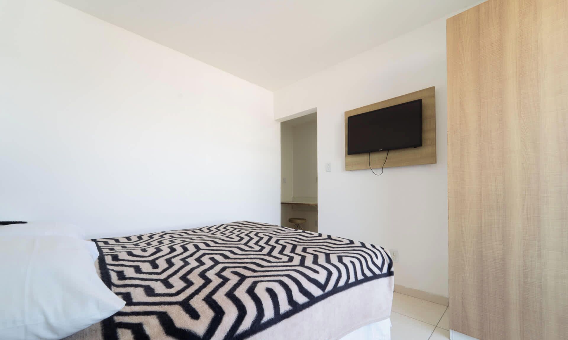 Un dormitorio moderno con una cama, un televisor de pantalla plana montado en la pared y un armario de madera.