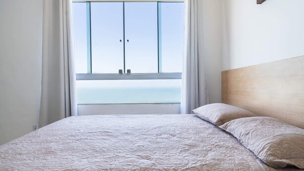 Ein Schlafzimmer mit Bett, einem Fenster mit Vorhängen und Meerblick.