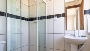 Ein Badezimmer mit Duschkabine aus Glas, einem weißen Waschbecken und einem Spiegel darüber.