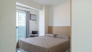 A hotel room with a bed, a chair, a window with curtains, and a wall-mounted air conditioning unit. - Apartamento no Centro de Macae Proximo a Praia (Macaé)