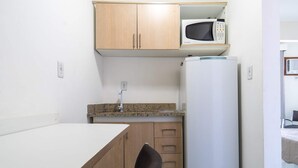 A compact kitchenette with a microwave, a refrigerator, a sink, and a small dining table. - Apartamento no Centro de Macae Proximo a Praia (Macaé)