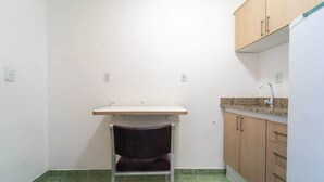 A small, compact kitchen with a single countertop, a chair, and wooden cabinets. - Apartamento no Centro de Macae Proximo a Praia (Macaé)
