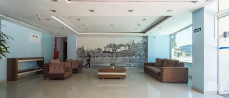 A modern lobby with a large mural, two sofas, a coffee table, and a reception desk.
