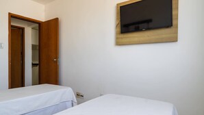Ein Schlafzimmer mit zwei Einzelbetten, einer Holztür und einem an der Wand befestigten Fernseher.